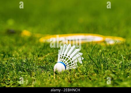 Weiße Federball Nahaufnahme in einer grünen Wiese mit gelbem Badminton Schläger vor verschwommenem Hintergrund Stockfoto