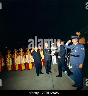 Reise in die westlichen Staaten: Honolulu, Hawaii, Ankunft am Honolulu International Airport, 9:10pm Uhr. Präsident John F. Kennedy (rechts, absteigende Flugzeugtreppe) schüttelt die Hände mit Gouverneur von Hawaii, John A. Burns, bei seiner Ankunft am Honolulu International Airport in Honolulu, Hawaii; Senator Daniel Inouye (Hawaii) steht links von Gouverneur Burns. Vertreter Spark M. Matsunaga (Hawaii) steigt Flugzeugtreppe hinter Präsident Kennedy; Naval Aide zum Präsidenten, Kapitän Tazewell T. Shepard, steht im Hintergrund in der Mitte. Mehrere nicht identifizierte Frauen stehen links (mit Blume leis); zwei uniden Stockfoto