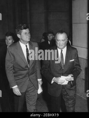 Ansprache an die Abschlussklasse, FBI National Academy, 11:26am Uhr. Präsident John F. Kennedy geht mit dem Direktor des Federal Bureau of Investigation (FBI), J. Edgar Hoover, während der Abschlussübungen der FBI National Academy. Agenten des Geheimdienstes des Weißen Hauses, Jerry Behn (links) und Emory Roberts (rechts), folgen ihm. Departmental Auditorium, Washington, D.C. Stockfoto