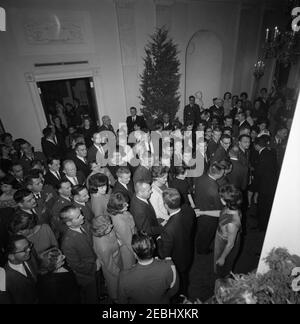 Weihnachtliche Party der Mitarbeiter des Weißen Hauses im Ostsaal, 6:30pm Uhr. Präsident John F. Kennedy und First Lady Jacqueline Kennedy (beide in der Mitte rechts im Vordergrund, von oben gesehen) begrüßen die Gäste, die in der Cross Hall während einer Weihnachtsfeier für das Personal des Weißen Hauses versammelt sind; Gäste füllen den Flur und in den Grünen Raum links. Ebenfalls im Bild: Air Force Aide to the President, Brigadier General Godfrey T. McHugh; White House Secret Service Agent, Clint Hill. White House, Washington, D.C. Stockfoto