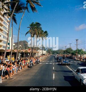 Reise nach Weststaaten: Honolulu, Hawaii, Autokolonne, 3:15pm Uhr. Präsident John F. Kennedy (im zweiten Auto) fährt in der Präsidentenlimousine (Lincoln-Mercury Continental Cabrio), während seine Autokolonne durch Honolulu, Hawaii reist; Senator Daniel Inouye (Hawaii) sitzt in der Limousine. Die Spitze des Diamantkopfes ist im Hintergrund links zu sehen. Auch abgebildet: White House Secret Service Agenten, Ron Pontius, Dennis R. Halterman, Charlie Kunkel und Bill Greer. Menschenmassen säumen die Straße. Stockfoto