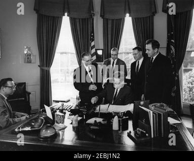 Bill Signing - Drainage of Wetlands, 10:15am. Präsident John F. Kennedy (am Schreibtisch sitzend) unterzeichnet eine Änderung des Bodenschutzgesetzes und des Hauszuteilungsgesetzes, um die Entwässerung von Feuchtgebieten zu begrenzen. Hinter Präsident Kennedy (L-R) stehen: Repräsentant Lester R. Johnson (Wisconsin); Stellvertretender Landwirtschaftsminister, John P. Duncan, Jr.; Repräsentant Henry S. Reuss (Wisconsin); Senator Eugene J. McCarthy (Minnesota). Ein nicht identifizierter Stenograf sitzt ganz links. Oval Office, White House, Washington, D.C. Stockfoto