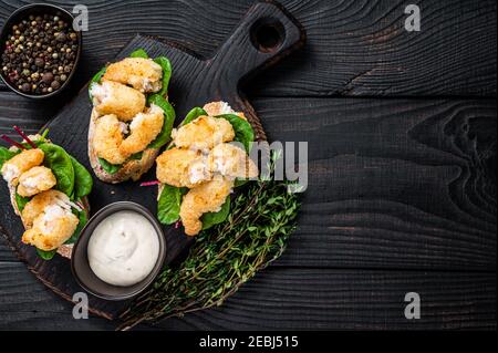 Toasts mit knusprig gebratenen Garnelen und grünem Salat auf einem Holzbrett. Schwarzer Holzhintergrund. Draufsicht. Speicherplatz kopieren Stockfoto