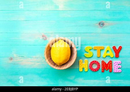 Wörter BLEIBEN ZU HAUSE und gelbe Zitrone in Holzschüsselteller auf türkisfarbenem Holz Hintergrund. Text BLEIBEN SIE HEIMAT von Holzbuchstaben und Obst in Platte Draufsicht. Kopieren Stockfoto