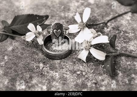 Schwarz und weiß von Silber alten Ringen auf einem Stein von biens Alba Blumen umgeben, die Form eines Herzens ist auf einem von ihnen geschnitzt Stockfoto