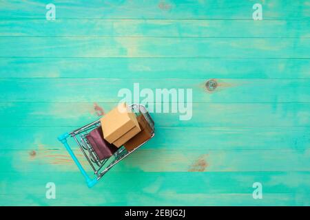 Warenkorb gefüllt mit Boxen auf Vintage-Holz Hintergrund. Kleiner Trolley auf türkisfarbenem Holzbrett. Draufsicht, Kopierbereich. Stockfoto