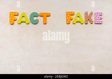 Wörter TATSACHE und GEFÄLSCHTE Formen von bunten Holzbuchstaben auf beigem Holz Hintergrund. Inschrift Tatsache oder Fälschung aus Holzbuchstaben. Fakt oder gefälschtes Konzept Stockfoto