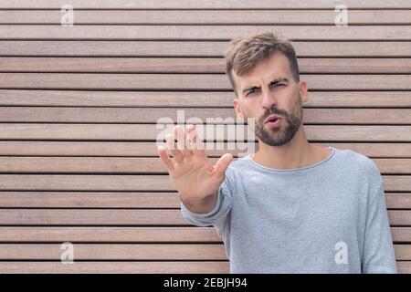 Mann zeigt mit seiner Hand Abstand auf Holzplanken Hintergrund zu halten. Kerl hält Abstand mit der Hand und sagt nein Sicheres Leben vor Coronavirus. Soc Stockfoto