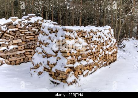 Holzstapel im Winter. Viele gehackte Baumstämme. Haufen Feuerholz bedeckt mit Schnee. Brennholz unter dem Schnee.Brennstoff Holz. Stockfoto