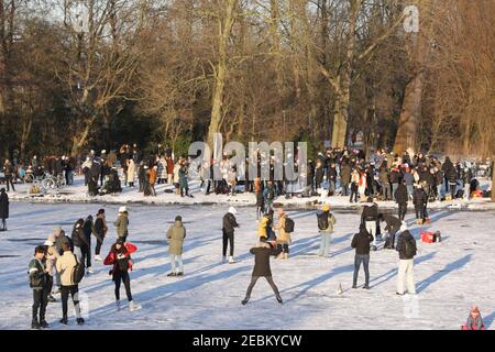 Am sonnigen Nachmittag im Vondelpark am 12. Februar 2021 in Amsterdam, Niederlande, treffen sich die Menschen beim Schlittschuhlaufen auf dem gefrorenen Kanal. Die Holländer Stockfoto