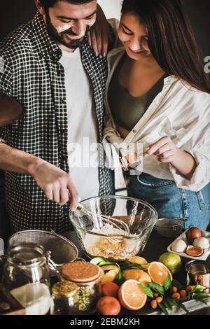 Süßes junges Familienpaar kochend zusammen in der Küche. Junge kaukasische Mann und Brünette Frau mit Gesichtern in Mehl Umarmung gebeizt, lachen und machen Teig für das Backen Zitruskuchen. Valentinstag, Hobbys zu Hause Stockfoto