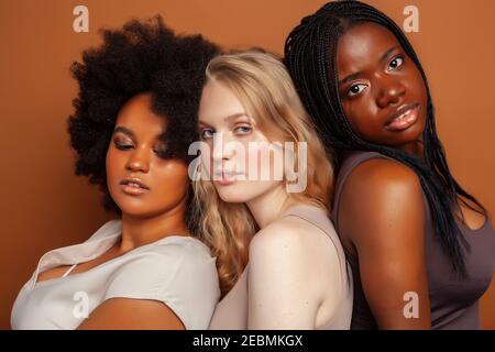 Junge hübsche kaukasische, afro, skandinavische Frau posiert fröhlich zusammen auf braunem Hintergrund, Lifestyle diverse Nationalität Menschen Konzept Stockfoto