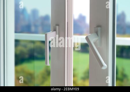 Schiebetür eines Balkons. Nahaufnahme des Schlosses an der Tür mit Blick auf die Stadt im Hintergrund. Weiße PVC-Tür mit Doppelglas. Stockfoto