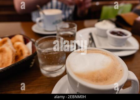 Cafeteria Tisch mit zwei schaumigen Latten, Toast mit Frischkäse und Marmelade, begleitet von zwei Schlucken von Mineralwasser . Buenos Aires - Argentinien Stockfoto