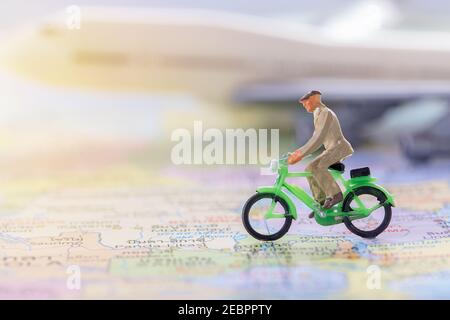 Miniatur Menschen - Figur Geschäftsmann Radfahren auf der Weltkarte mit verschwommenem weißen Flugzeug Hintergrund. Business Finance und Reisekonzept. Stockfoto