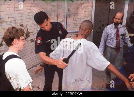 Austin Texas USA, um 1997: Ein Schulpolizist verwendet einen Metalldetektor, während ein Lehrer Rucksäcke inspiziert, wenn die Schüler zu Beginn des Schultages ihre Mittelschule betreten. ©Bob Daemmrich Stockfoto