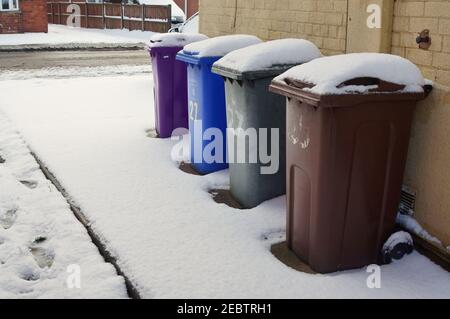 Vier verschiedene schneebedeckte Abfallbehälter an einer Hauswand bei kaltem Winterwetter Stockfoto