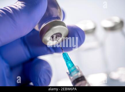 Nahaufnahme von Handschuhen mit Covid-19-Impfstofffläschchen und Spritze Stockfoto