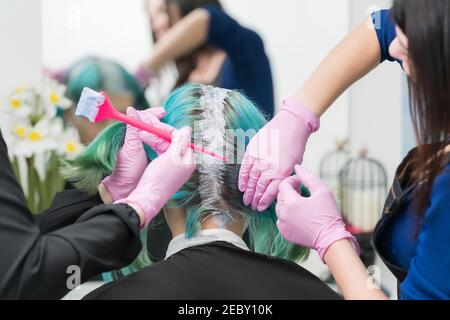 Prozess der Haarfärbung im Schönheitssalon. Zwei professionelle Friseure, die Farbe auf das Haar auftragen, während sie Haarwurzeln bleichen Stockfoto