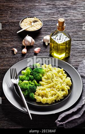 Brokkoli Kartoffelpüree mit gehackten Mandeln bestreut serviert mit gedünsteten Brokkoli blüsst auf einem schwarzen Teller auf einem dunklen Holz Tabelle Stockfoto