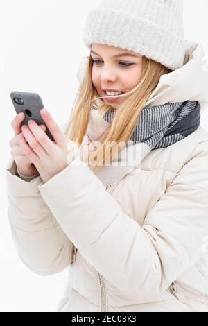 Cute kaukasischen Mädchen im Winter weiße Kleidung verwendet Handy Zur Navigation in der Winterstadt Stockfoto