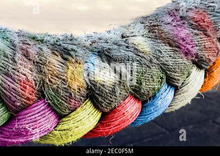 Nahaufnahme eines starken Seils, das in der Luft hängt, teilweise in gutem Zustand und bunt, teilweise abgenutzt mit verblassten Farben. Stockfoto