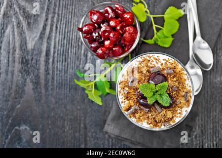 Dessert Schwarzer Wald von Kirschen, Schokoladenkeks und weichen Quark mit Sahne im Glas auf einer Serviette, Minze, Beeren in einer Schüssel und Löffel auf wo Stockfoto