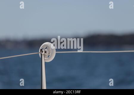 Blick über einen Geländerpfosten auf einem Segelboot, mit selektivem Fokus, mit unscharfen Blick auf Meer und Land. Segeln oder Bootfahren Hintergrund mit Kopieplatz Stockfoto