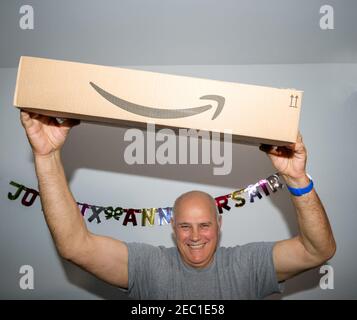 Paris, Frankreich - Oct 10, 2019: Happy Senior Mann lächelnd tanzend, während er ein großes neues Amazon Prime Paketlogotyp mit dem lächelnden Pfeil hält - Happy Birthday Signage an der Wand im Hintergrund Stockfoto