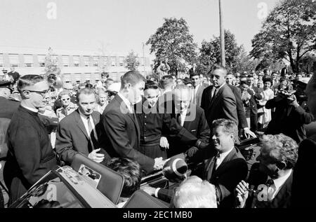 Kongreßfeldzug Reise: Cleveland, Ohio, Ankunft, Rallye, Autokolonne, Abfahrt. Präsident John F. Kennedyu2019s Autokolonne hält vor der St. Edward High School in Lakewood, Ohio, während einer Kongresskampagne Reise; Präsident Kennedy erhält einen Fußball im Namen der Studentenschaft von Senior Class Präsident Robert Cutter, und Rektor, Bruder Charles Krupp. Ebenfalls im Bild: Repräsentant Michael J. Feighan aus Ohio (auf dem Vordersitz des Cabrios, Rücken zur Kamera); Senator Frank Lausche aus Ohio (auf dem Rücksitz mit Präsident Kennedy); Bruder Florentius Schu (ganz links stehend); Cha Stockfoto