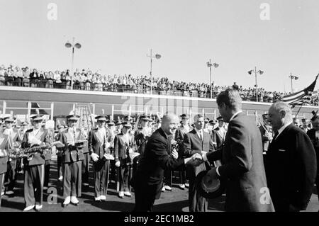 Kongreßfeldzug Reise: Cleveland, Ohio, Ankunft, Rallye, Autokolonne, Abfahrt. Präsident John F. Kennedy schüttelt sich bei der Ankunft am Cleveland Hopkins Airport in Cleveland, Ohio, während einer Wahlkampfreise des Kongresses die Hände mit einem unbekannten Mann. Der Vorsitzende der Demokratischen Partei des Landkreises Cuyahoga, Ray T. Miller, steht ganz rechts. Eine Band von der St. Edward High School in Lakewood, Ohio, steht dahinter, ein großes Publikum auf dem Dach schaut auf. Stockfoto