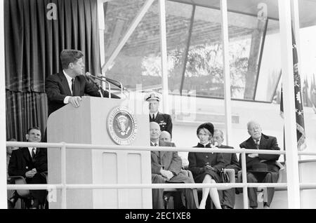 Dedication Ceremonies, Dulles International Airport, 11:12am Uhr. Präsident John F. Kennedy (auf dem Rednerpult) hält Bemerkungen bei der Einweihungszeremonie für den internationalen Flughafen Dulles, benannt nach dem verstorbenen Staatssekretär John Foster Dulles. Ebenfalls auf der Plattform speakersu2019 abgebildet: Vertreter Oren Harris von Arkansas (hinter Rednerpult); ehemaliger Präsident, General Dwight D. Eisenhower; Naval Aide to the President, Captain Tazewell T. Shepard, Jr. (stehend); Aline B. Saarinen (Witwe des Architekten für den Flughafen, Eero Saarinen); ehemaliger Direktor der Central Intelligence Agency (CIA), Allen Stockfoto