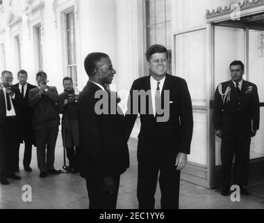 Mittagessen zu Ehren von Sylvanus Olympio, Präsident von Togo, 1:00pm Uhr. Präsident John F. Kennedy besucht mit Präsident von Togo, Sylvanus Olympio (links), nach der Ankunft von Präsident Olympiou2019s im Weißen Haus für ein Mittagessen zu seinen Ehren. Air Force Aide to President Kennedy, Brigadier General Godfrey T. McHugh, steht in der Tür auf der rechten Seite; Fotografen, darunter Wochenschau-Fotograf für United Press Movietone, Thomas J. Craven, Sr., und Filmfotograf für Columbia Broadcasting System (CBS), Tom J. Craven, Jr., stehen auf der linken Seite. North Portico, White House, Washington, D.C. Stockfoto