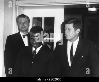 Treffen mit Sylvanus Olympio, Präsident von Togo, 2:53pm Uhr. Präsident John F. Kennedy und Präsident von Togo, Sylvanus Olympio (Mitte), verlassen das Weiße Haus nach ihrem Treffen und Mittagessen. Staatssekretär für afrikanische Angelegenheiten, G. Mennen u201cSoapyu201d Williams, steht hinter Präsident Olympio. Eingang im Westflügel, weißes Haus, Washington, D.C. Stockfoto