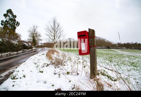 Roter britischer Briefkasten, Winterzeit. Pole montiert englischen Briefkasten auf dem Land. Winter, verschneite Tage Stockfoto