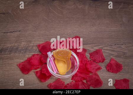 Parfümiertes Rosenwasser und Rosenblüte aus Seife in Glaswaren auf Holztisch mit Rosenblättern. Hintergrund für den Kopierbereich. Stockfoto