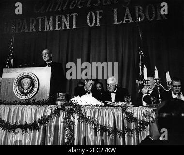 Ansprache bei der Zeremonie zum 50th. Jahrestag des Arbeitsministeriums, 10:26pm Uhr. Präsident John F. Kennedy (raucht eine Zigarre) nimmt an einem Abendessen Teil, das den 50th. Jahrestag des Arbeitsministeriums feiert; Arbeitsminister W. Willard Wirtz gibt Bemerkungen vom Rednerpult ab. Sitzend (L-R): Präsident Kennedy; Präsident der American Federation of Labor and Congress of Industrial Organizations (AFL-CIO), George Meany; Postmaster General, J. Edward Day (hinter Candelabra); ehemaliger Sekretär der Arbeit, James P. Mitchell. Sheraton Park Hotel, Washington, D.C. Stockfoto