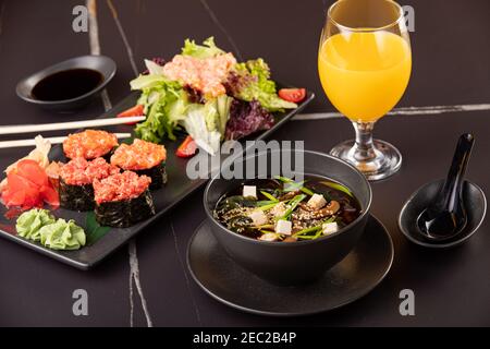 Japanisches Essen, Sushi, Brötchen, Suppe, Salat auf schwarzem Hintergrund Stockfoto