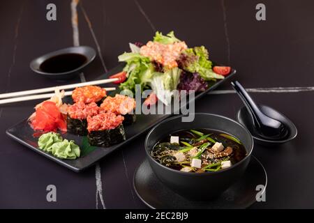 Japanisches Essen, Sushi, Brötchen, Suppe, Salat auf schwarzem Hintergrund Stockfoto