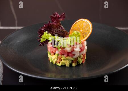 Tartar aus frischem rohem Thunfisch mit Gewürzen in Nahaufnahme auf einem Teller. Horizontal auf schwarzem Hintergrund Stockfoto