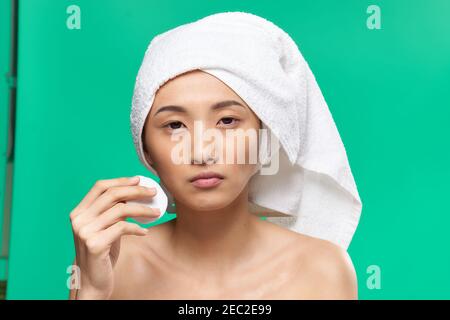 Frau mit einem Handtuch auf dem Kopf wischt ihr Gesicht Mit einem Wattepad Grün Hintergrund Stockfoto