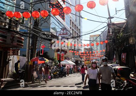 Ongpin St., Binondo, Manila, Philippinen. Februar 2021, 13th. Menschen mit Gesichtsmasken und Gesichtsschilden gehen in Ongpin, Binondo, während der Feier des chinesischen Neujahrs durch die mit chinesischen Laternen geschmückten Straßen. Binondo ist als das älteste chinatown der Welt bekannt, die meisten Feiern wie Drachen- und Löwentänze wurden aufgrund der Pandemie abgesagt. Kredit: Majority World CIC/Alamy Live Nachrichten Stockfoto