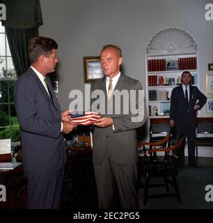 Besuch von Astronaut John Herschel Glenn, Jr. Präsident John F. Kennedy erhält ein Geschenk einer amerikanischen Flagge von Astronaut Oberstleutnant John H. Glenn, Jr. (rechts); LT. Col. Glenn trug die Flagge in seinem Raumanzug während seines Orbitalflugs an Bord von Mercury-Atlas 6, auch bekannt als Friendship 7. Sonderassistent des Präsidenten, Kenneth P. Ou0027Donnell, steht im Hintergrund. Oval Office, White House, Washington, D.C. Stockfoto