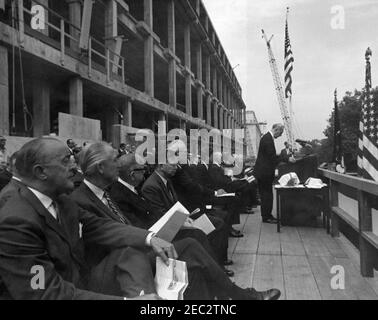 Grundsteinlegung, Bürogebäude Rayburn House, 10:28am Uhr. Der Sprecher des Repräsentantenhauses und Vorsitzender der House Office Building Commission, John W. McCormack aus Massachusetts (am Rednerpult), hält bei der Grundsteinlegung für das Rayburn House Office Building, das dem verstorbenen Sprecher des Hauses, Sam Rayburn, gewidmet ist, Bemerkungen; Präsident John F. Kennedy sitzt im Zentrum. Ebenfalls im Bild: Repräsentantin Leslie C. Arends (Illinois); Repräsentantin Clarence Cannon (Missouri); Repräsentant Carl Albert (Oklahoma); Oberrichter des Obersten Gerichtshofs, Earl Warren; Mitglied Stockfoto