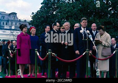 Ankunftszeremonie für Konrad Adenauer, Bundeskanzler der Bundesrepublik Deutschland, 10:45am Uhr. Präsident John F. Kennedy (bei Mikrofonen) hält bei den Ankunftszeremonien zu Ehren des Bundeskanzlers der Bundesrepublik Deutschland, Dr. Konrad Adenauer, eine Rede. Auf der Überprüfungsplattform: Bundeskanzlerin Adenauer; First Lady Jacqueline Kennedy; Libeth Werhahn, Tochter von Bundeskanzler Adenauer; Außenminister der Bundesrepublik Deutschland, Gerhard Schru00f6der; Dolmetscher für das deutsche Außenministerium, Heinz Weber; Vorsitzender der Generalstabschefs, General Maxwell D. Taylor; Botschafter der Bundesrepublik Deutschland, Karl Heinrich Knappstei Stockfoto