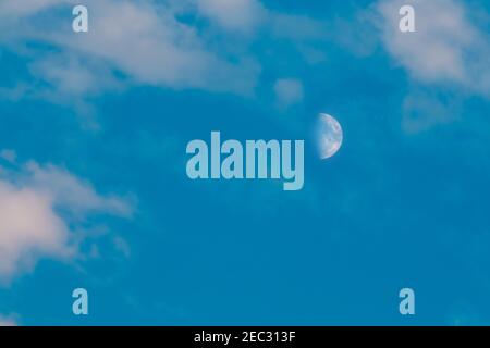 Halb abnehmender Mond auf dem Hintergrund des wolkigen blauen Himmels in Tagsüber Stockfoto