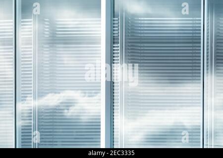 Wolken und Himmel spiegeln sich in den Fenstern mit Lamellen des modernen Bürogebäudes in der Stadt, verschwommener Effekt Stockfoto