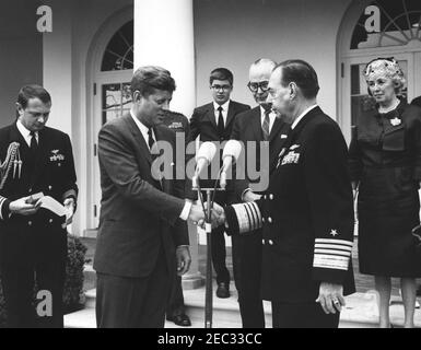 Übergabe der Distinguished Service Medal (DSM) an ADM. Robert Dennison, 12:00pm Uhr. Präsident John F. Kennedy schüttelt sich die Hände, als er bei der Übergabe der Distinguished Service Medal (DSM) an Admiral Dennison den U.S. Navy Admiral, Robert L. Dennison, in den Ruhestand verabschiedet. Von links nach rechts: Naval Aide to the President, Captain Tazewell Shepard; Präsident Kennedy; nicht identifizierter Junge (im Rücken); Sekretär der Marine, Fred Korth; Admiral Dennison; nicht identifizierte Frau. Rose Garden, White House, Washington, D.C. Stockfoto