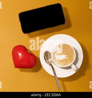 tasse Kaffee mit Schokolade, rotes Herz, Telefon auf einem Tisch Stockfoto