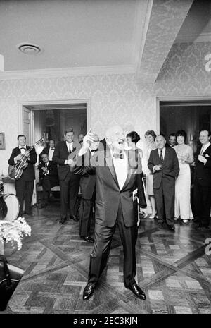 Ausflug nach New York City: Empfang, Arthur Krim Residence. Entertainer Jimmy Durante tritt bei einem Abendempfang in der Residenz von Arthur B. Krim und Dr. Mathilde Krim in New York City, New York auf; Präsident John F. Kennedy steht links im Hintergrund. Ebenfalls im Bild: Vizepräsident Lyndon B. Johnson; Julie Robinson Belafonte; Eunice Kennedy Shriver; Herr Krim; Dekan des Pressecorps des Weißen Hauses und Reporter von United Press International (UPI), Merriman u0022Smittyu0022 Smith; Schauspieler und Sängerin Shirley MacLaine. Stockfoto